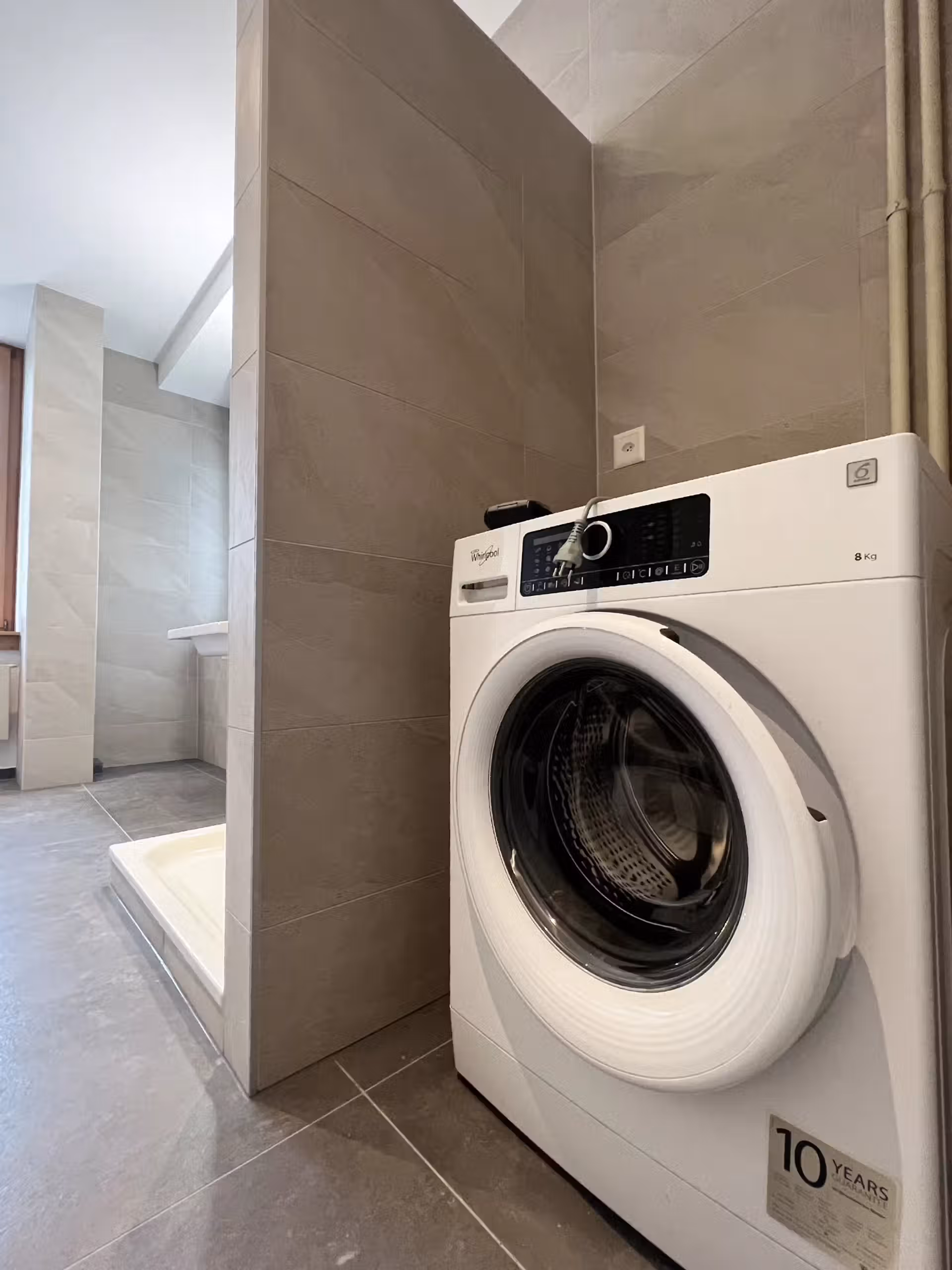 Lave-linge Whirlpool blanc avec écran numérique et hublot transparent, situé dans une salle de bain contemporaine.